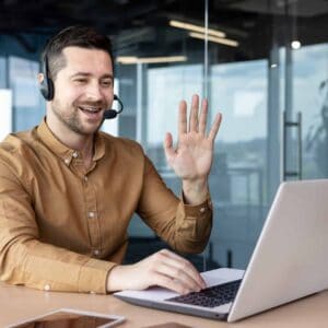 A young businessman wearing a headset smiles and talks on a video call.