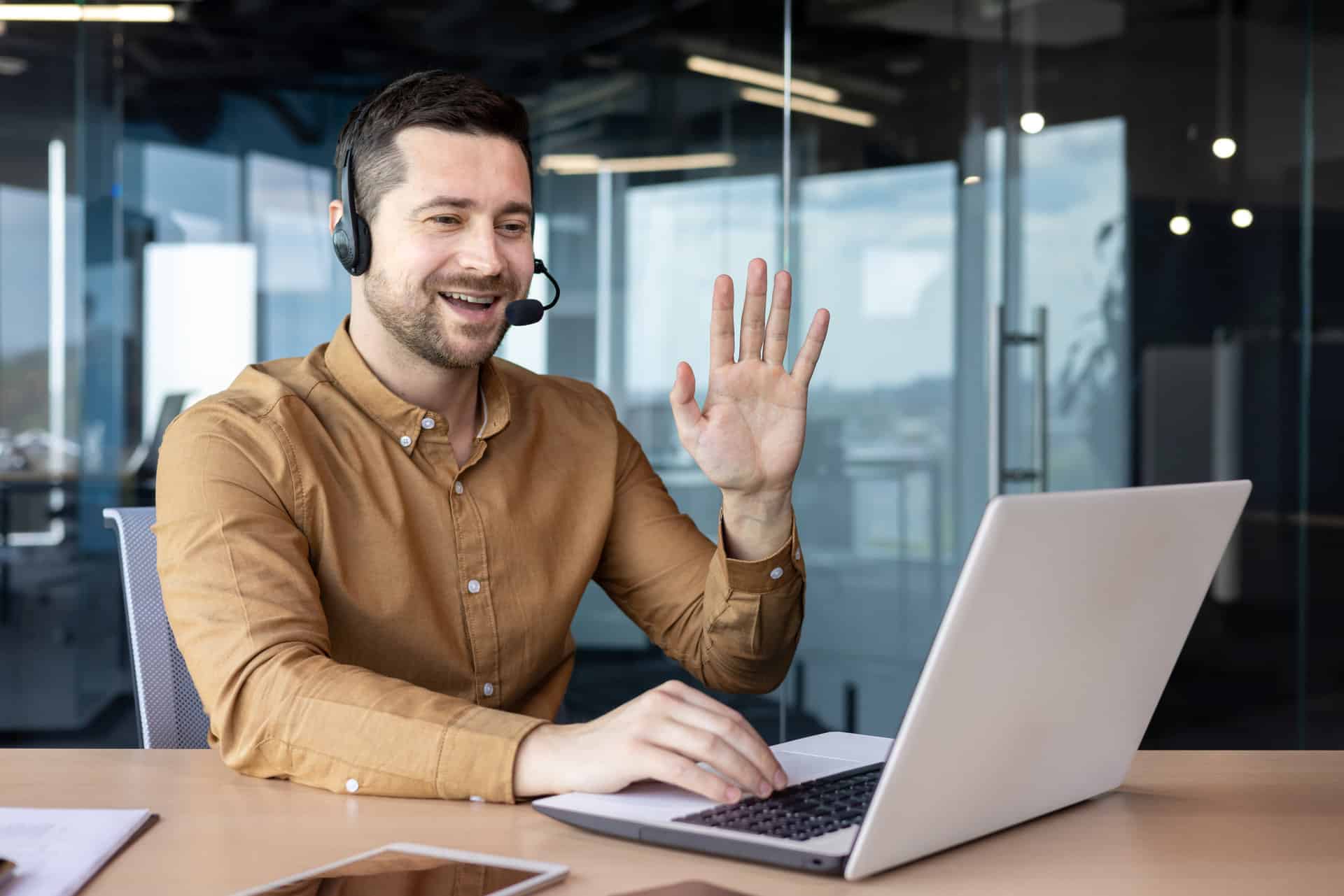 A young businessman wearing a headset smiles and talks on a video call.