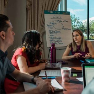 People sit in discussion around a conference table with a flip chart in the background.