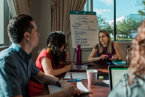 People sit in discussion around a conference table with a flip chart in the background.