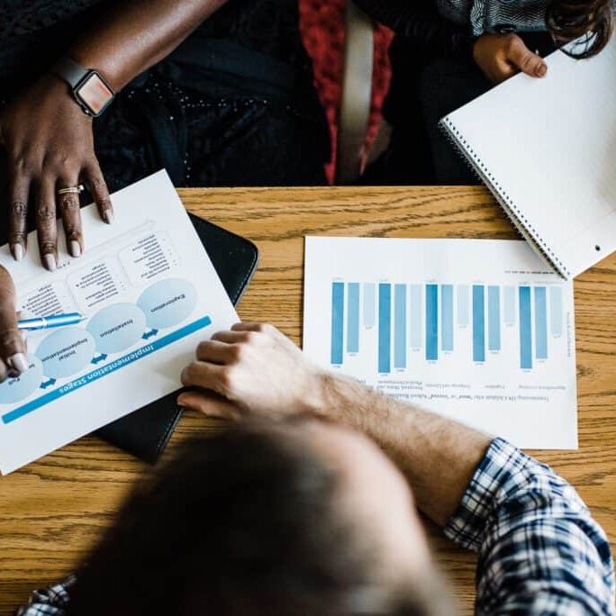 Hands of people at a table, collaborating on data analysis and reviewing data graphs